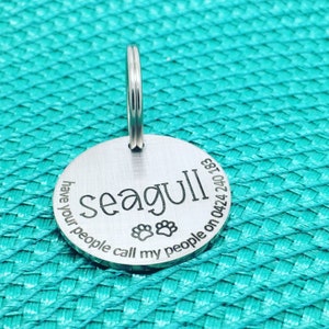 May include: A round, silver pet tag with the name "seagull" in a bold font. The tag includes paw prints and the phrase "have your people call my people on 0424 240 183". A silver ring is attached for easy attachment to a collar.