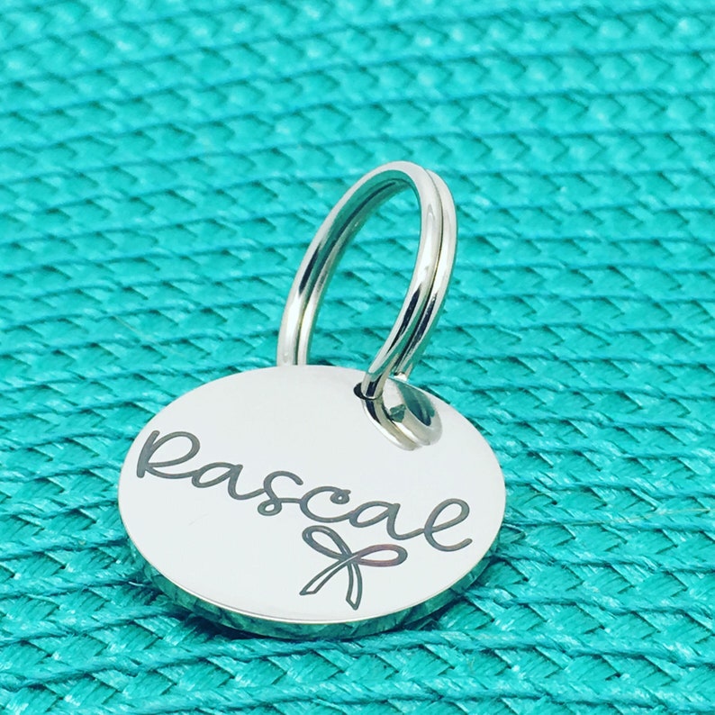 May include: Silver key chain with a round tag engraved with the name "Pascal" and a small ribbon.