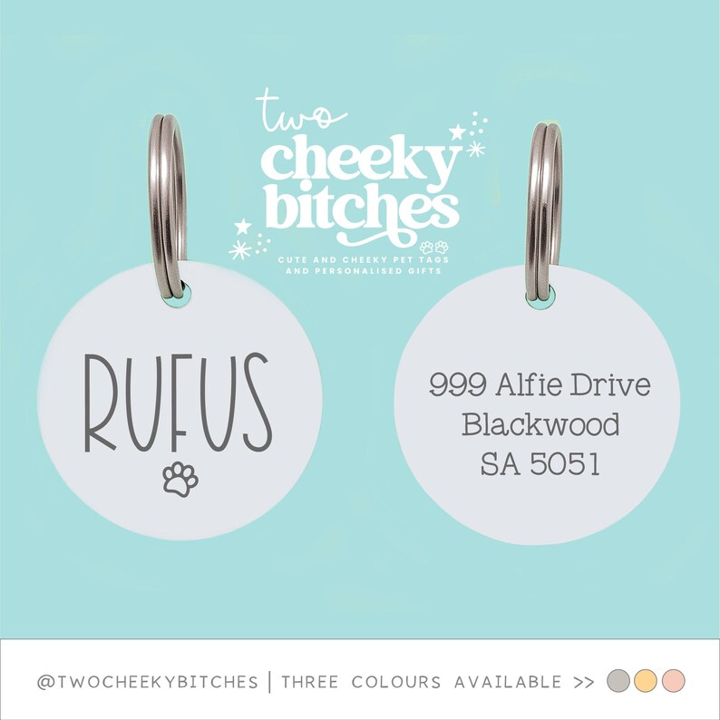 May include: Two white pet tags with silver rings. One tag says "RUFUS" with a paw print, the other has an address. The text "two cheeky bitches" is at the top, with "CUTE AND CHEEKY PET TAGS AND PERSONALISED GIFTS" below.