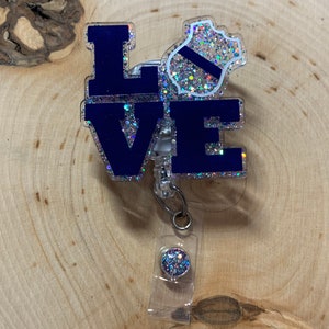 May include: A blue and silver glitter badge holder with the word "LOVE" and a police badge design. The badge holder is attached to a clear retractable badge reel with a silver and blue glitter button.