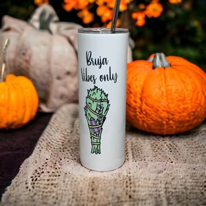 May include: White stainless steel tumbler with a black and white graphic of a bundle of herbs and crystals. The text "Bruja Vibes only" is printed on the tumbler.
