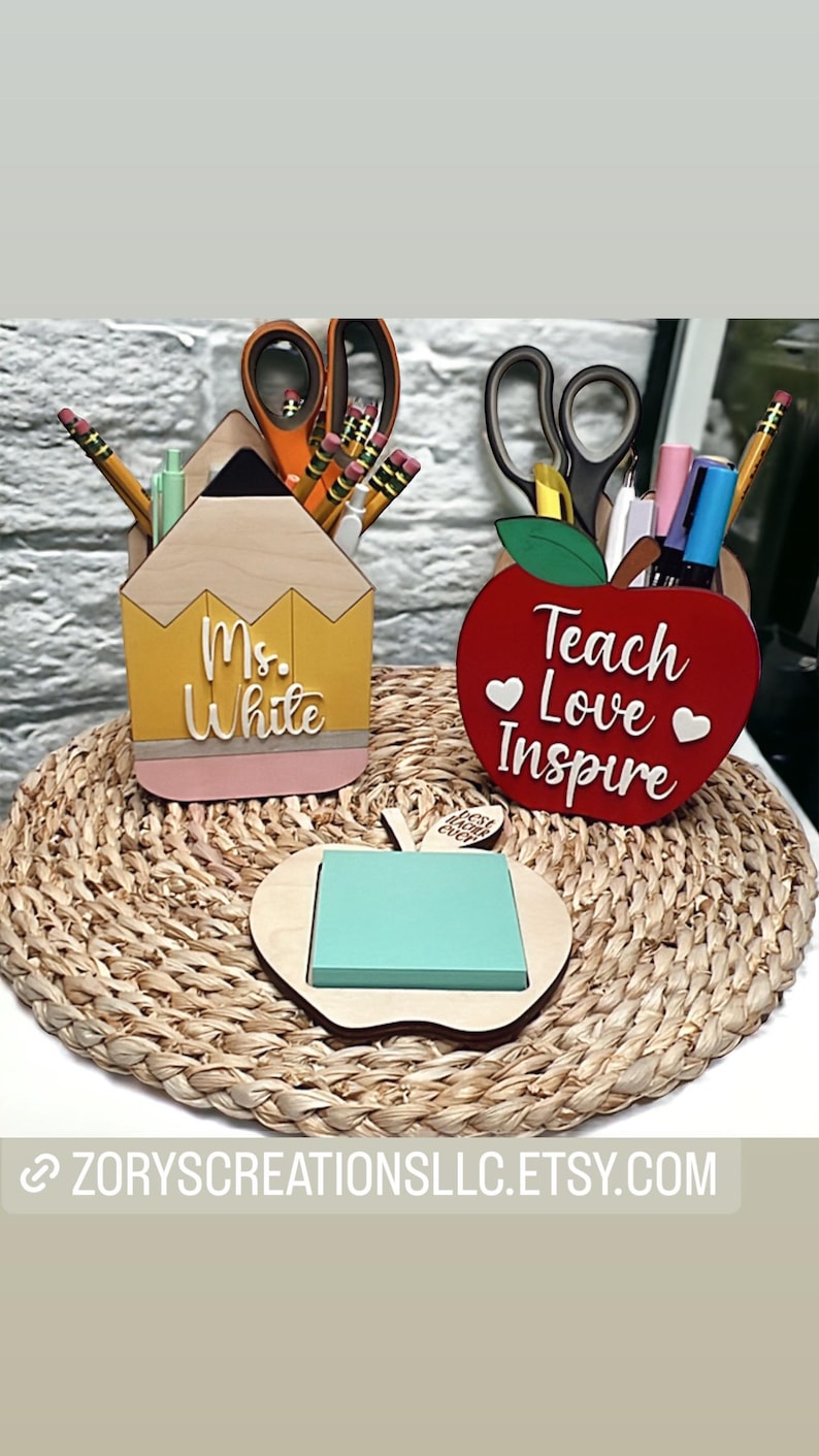 May include: Two wooden desk organizers, one shaped like a pencil and the other like an apple. The pencil organizer is yellow and pink and says "Ms. White". The apple organizer is red and says "Teach Love Inspire". Both organizers have a space for pens, pencils, and other office supplies.