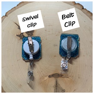 May include: Two teal blue glitter retractable badge holders with a white swivel clip and a silver belt clip. The text "Swivel clip" and "Belt Clip" are written on white paper.