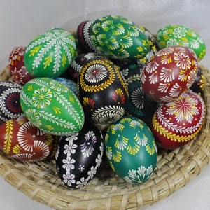 May include: A collection of intricately decorated Easter eggs in a woven basket. The eggs are painted in various colors, including green, red, black, and white, with intricate floral and geometric designs.