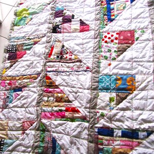 Könnte beinhalten: Eine weiße Steppdecke mit Patchwork-Muster. Die Steppdecke besteht aus verschiedenen bunten Dreiecken und Quadraten. Die Steppdecke ist mit weißem Garn gesteppt.