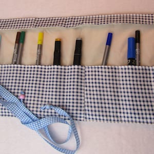 Könnte beinhalten: Eine blaue und weiße Gingham-Stoffrolle mit einer Schleifenverschlusses. Die Rolle ist mit einer Vielzahl von farbigen Markern gefüllt.