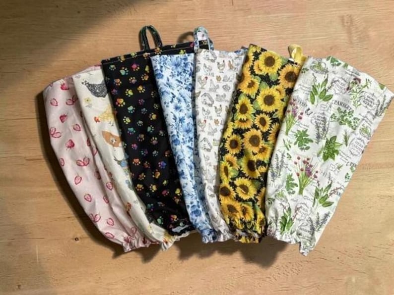 May include: A collection of six fabric bags with hanging loops, featuring various patterns including pink strawberries, chickens, colorful paw prints, blue floral designs, yellow sunflowers, and green herbs on white and black backgrounds.