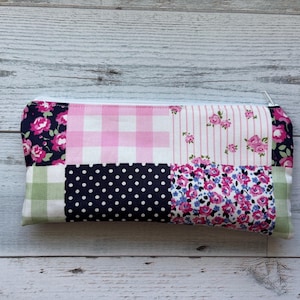 Puede incluir: Un estuche rectangular con un dise&ntilde;o de patchwork. El estuche presenta varios patrones de tela, incluyendo cuadros rosas, estampados florales, lunares y rayas. Una cremallera blanca recorre el borde superior. El estuche mide aproximadamente 20 cm de largo.