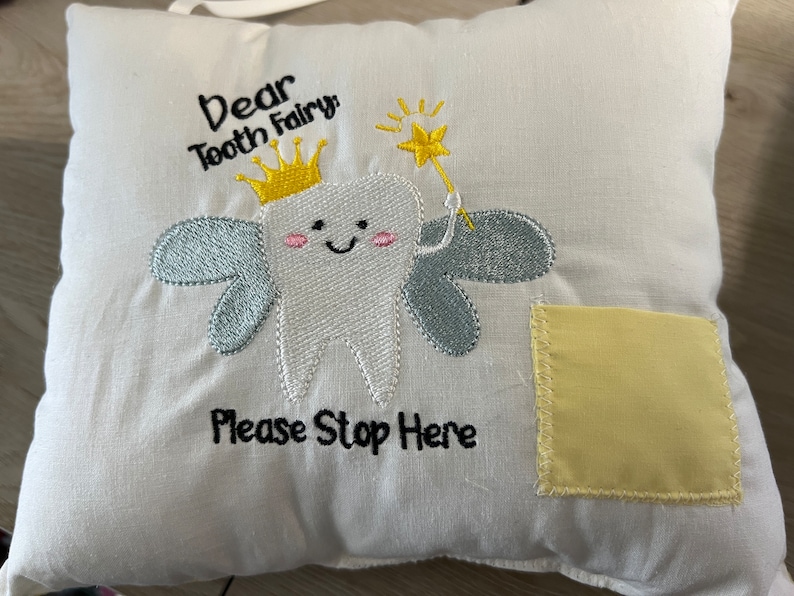 May include: White pillow with embroidered tooth fairy design. The tooth fairy is a white tooth with a crown, wings, and a wand. The pillow says "Dear Tooth Fairy, Please Stop Here".