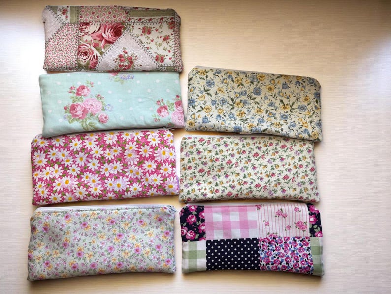 Puede incluir: Una colecci&oacute;n de ocho bolsas rectangulares de tela con estampados florales y patchwork. Las bolsas presentan varios colores, incluyendo rosa, azul y blanco, con dise&ntilde;os de rosas, margaritas y otros motivos florales. Las bolsas est&aacute;n dispuestas sobre una superficie clara.