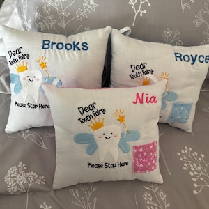 May include: Four white pillowcases with embroidered tooth fairy designs. Each pillowcase has a different name: Brooks, Royce, Nia, and Dear Tooth Fairy. The pillowcases have a blue and pink design with a tooth fairy holding a wand.