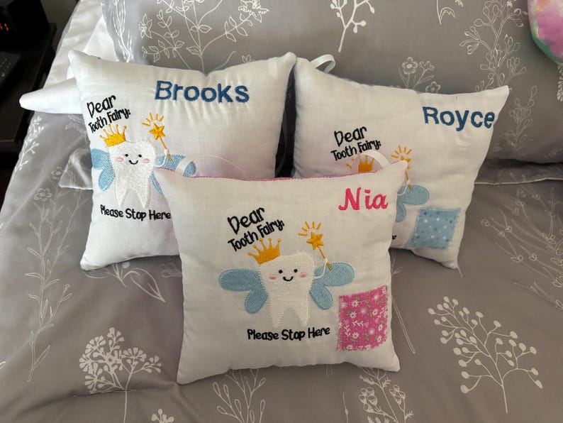 May include: Four white pillowcases with embroidered tooth fairy designs. Each pillowcase has a different name: Brooks, Royce, Nia, and Dear Tooth Fairy. The pillowcases have a blue and pink design with a tooth fairy holding a wand.