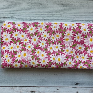 Puede incluir: Una bolsa rectangular con cremallera con un fondo rosa cubierto de margaritas blancas con centros amarillos. La bolsa est&aacute; hecha de tela y tiene una cremallera blanca.