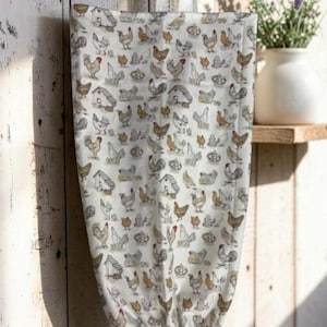 May include: A fabric bag with a white background featuring a repeating pattern of brown, grey, and white chickens, roosters, and small coops. The bag has a white fabric loop at the top for hanging and an elasticized opening at the bottom.