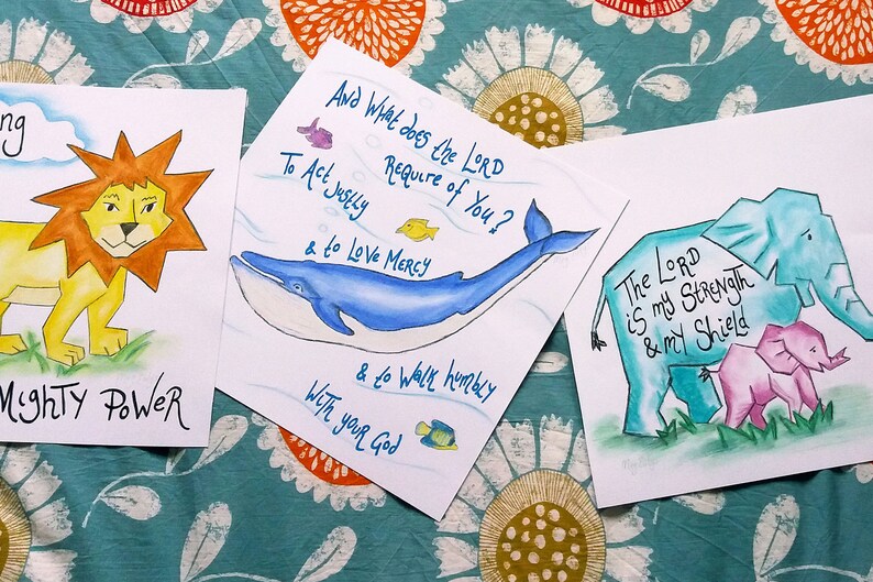 Puede incluir: Tres acuarelas con citas inspiradoras e ilustraciones de animales. La primera pintura presenta un le&oacute;n con el texto "Mighty Power". La segunda pintura presenta una ballena con el texto "And What does the LORD Require of You? To Act Justly & to Love Mercy & to Walk humbly With your God". La tercera pintura presenta un elefante y un elefante beb&eacute; con el texto "The LORD is my Strength & my Shield".