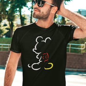 May include: Black t-shirt featuring a white, red, and yellow outline of a cartoon mouse. The shirt has short sleeves and a crew neck. The design is a minimalist illustration of a popular cartoon character.