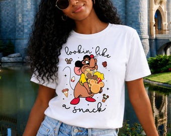 Puede incluir: Una camiseta blanca de manga corta con el gráfico de un ratón marrón sosteniendo varios aperitivos, con el texto "lookin' like a snack" escrito en cursiva negra, rodeado de pequeños iconos de helados, pretzels y gofres.