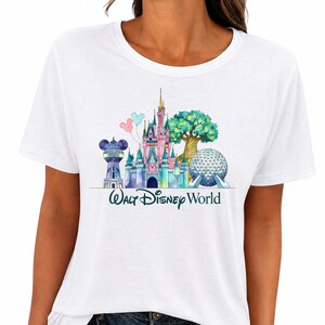 May include: A white short-sleeved t-shirt featuring a colorful watercolor graphic of the Walt Disney World landmarks, including the castle, the geodesic sphere, and the water tower, with the text Walt Disney World printed in dark teal below.