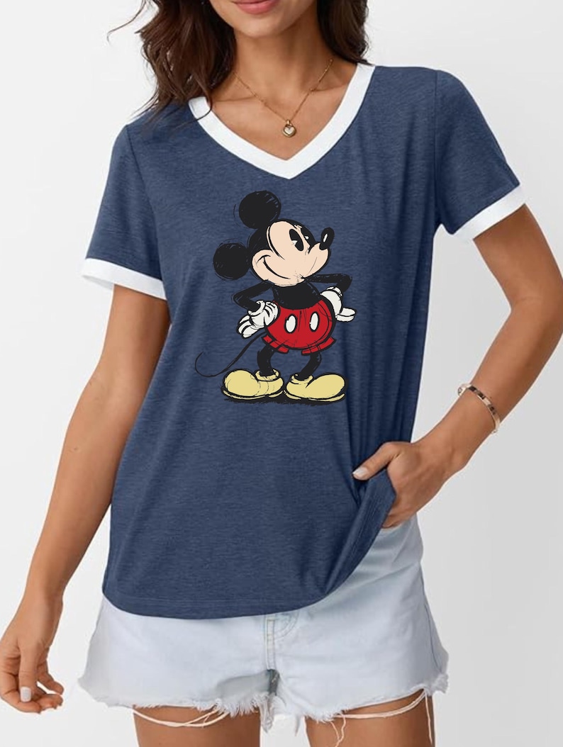 May include: Navy blue V-neck t-shirt with white trim featuring a graphic of Mickey Mouse. The cartoon character is in a classic pose, wearing red shorts, yellow shoes, and white gloves. A casual, comfortable top.