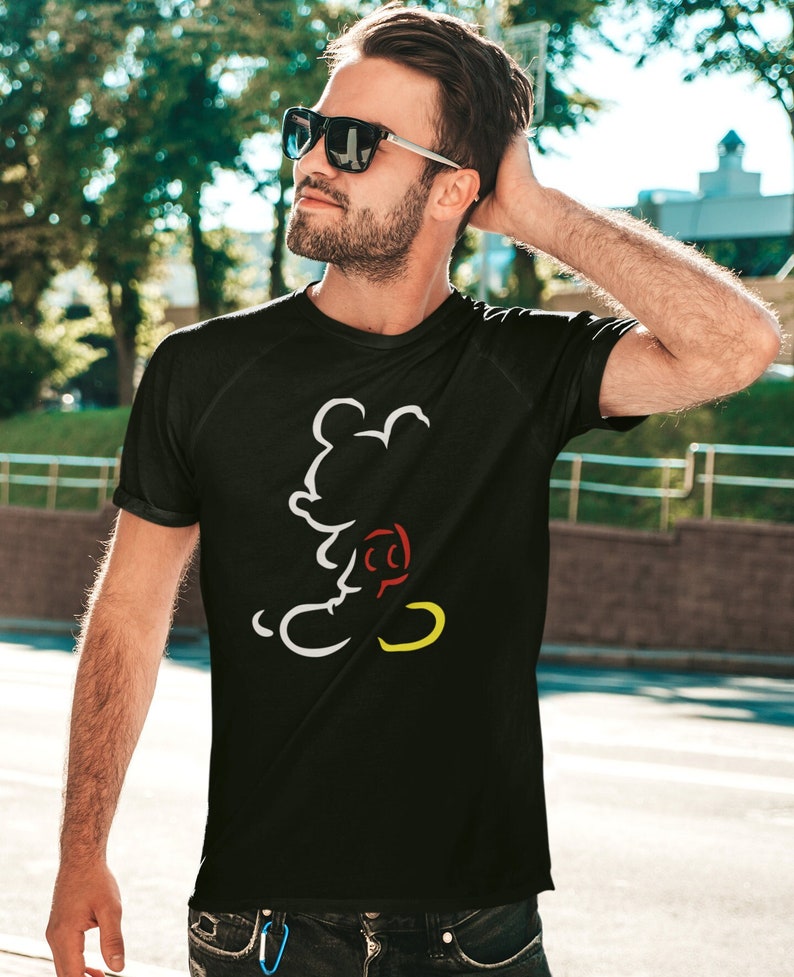 May include: Black t-shirt featuring a white, red, and yellow outline of a cartoon mouse. The shirt has short sleeves and a crew neck. The design is a minimalist illustration of a popular cartoon character.