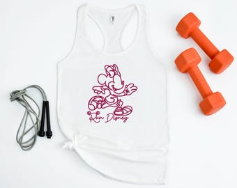 May include: White racerback tank top with a magenta graphic of a cartoon character and the text "Run Disney." Two orange dumbbells and a gray jump rope are also in the image.