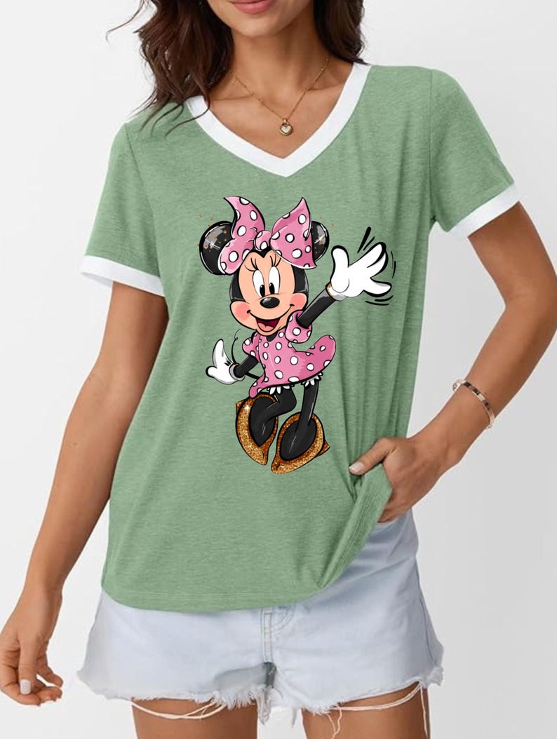 K&ouml;nnte beinhalten: Gr&uuml;nes V-Ausschnitt-T-Shirt mit wei&szlig;em Besatz mit einem Minnie Mouse-Motiv. Minnie tr&auml;gt ein rosa gepunktetes Kleid und eine Schleife mit goldenen Glitzerschuhen. Das Shirt hat einen l&auml;ssigen Stil.