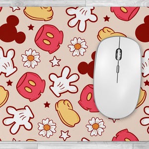 May include: A pink and white mouse pad with a repeating pattern of Mickey Mouse hands, Mickey Mouse heads, and red and yellow polka dots. A white computer mouse is on top of the mouse pad.