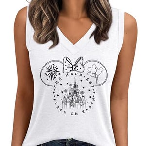 May include: White V-neck tank top with a black and white graphic. The graphic features a castle, fireworks, balloons, and a bow, with the text "THE HAPPIEST PLACE ON EARTH" in a circular design. The tank top is sleeveless.