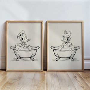 May include: Two framed black and white prints featuring Donald Duck and Daisy Duck in bathtubs. The artwork has a minimalist style with a light background and wooden frames. The ducks are drawn in a classic cartoon style.