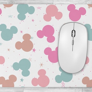 May include: A white computer mouse rests on a rectangular mousepad. The mousepad features a pattern of pink, teal, and peach-colored cartoon character heads and star shapes on a white background. The mouse is white with a black scroll wheel.