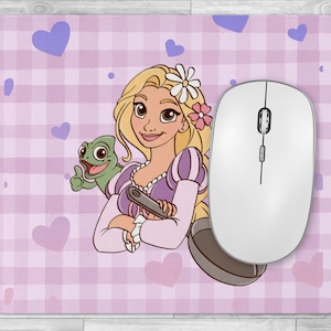 Peut inclure: Tapis de souris rectangulaire avec une illustration de princesse aux longs cheveux blonds, une grenouille verte et des cœurs violets sur un fond à carreaux roses. Une souris sans fil blanche est à droite.