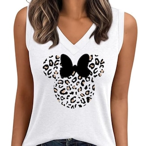 May include: White sleeveless top with a V-neck design. The top features a black bow and a Minnie Mouse head design with a leopard print pattern. The top is made of a soft material and is suitable for casual wear.