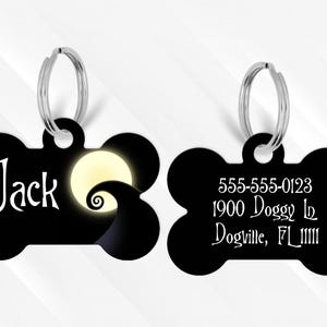 May include: Black bone-shaped pet tag with a silver ring. One side features the name "Jack" in white script with a moon and swirling design. The other side displays a phone number, address, and city in white script.