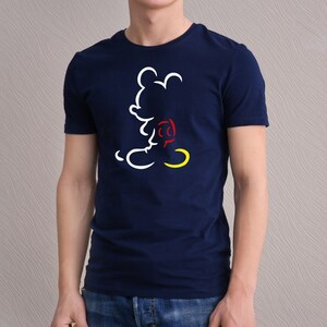 May include: Navy blue t-shirt featuring a white, red, and yellow outline of a cartoon mouse. The design is a minimalist illustration of the character. The shirt is a classic crew neck style.