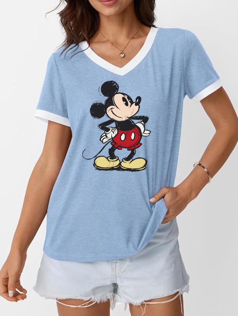 May include: Light blue V-neck t-shirt with white trim and a graphic of Mickey Mouse. The cartoon character is in a classic pose, wearing red shorts and yellow shoes. The shirt is a casual style.