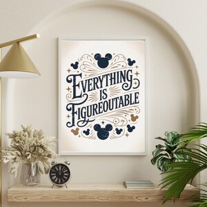 May include: Framed art print with the text "Everything is Figureoutable" in a decorative font, surrounded by Mickey Mouse silhouettes and stars. The artwork is in a white frame and is displayed on a wooden shelf with a clock and dried flowers.
