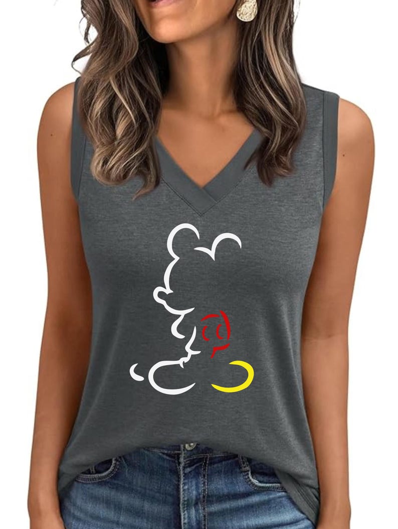 Puede incluir: Una camiseta sin mangas gris con cuello en V y un contorno blanco de Mickey Mouse. El pantal&oacute;n corto del personaje de dibujos animados es amarillo y su pajarita es roja. La camiseta se combina con unos vaqueros azules.