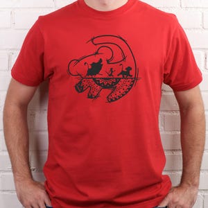 May include: A red t-shirt featuring a black graphic design. The design depicts a silhouette of characters from a popular animated film. The graphic includes a lion's head, and other characters. The shirt is made of a soft material.