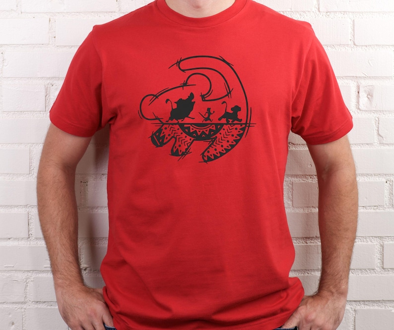 May include: A red t-shirt featuring a black graphic design. The design depicts a silhouette of characters from a popular animated film. The graphic includes a lion's head, and other characters. The shirt is made of a soft material.