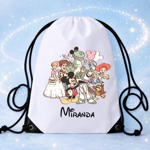 May include: A white drawstring backpack featuring a graphic print of Mickey Mouse, Buzz Lightyear, Woody, Jessie, Rex, Slinky Dog, and Bo Peep. The characters are holding balloons, and the name Miranda is printed in black text below the illustration.