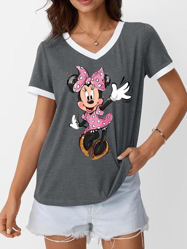 K&ouml;nnte beinhalten: Graues V-Ausschnitt-T-Shirt mit wei&szlig;em Besatz und Minnie Mouse-Grafik. Minnie tr&auml;gt ein rosa gepunktetes Kleid und eine Schleife mit goldenen Glitzerschuhen. Das T-Shirt hat einen l&auml;ssigen Stil.