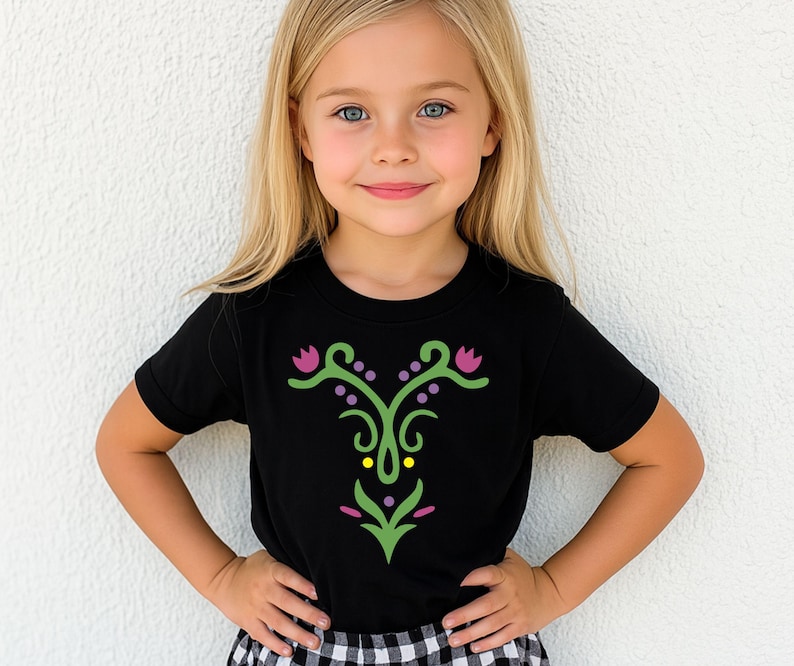 May include: Black short-sleeved t-shirt with a decorative floral design in green, purple, and yellow. The design is centered on the front of the shirt. The shirt is worn by a young child.