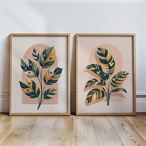 May include: Two framed art prints featuring stylized botanical illustrations. Each print showcases a plant with green, yellow, and blue leaves, accented with Mickey Mouse silhouettes. The background is a soft peach color with an arch design, all within a light wood frame.