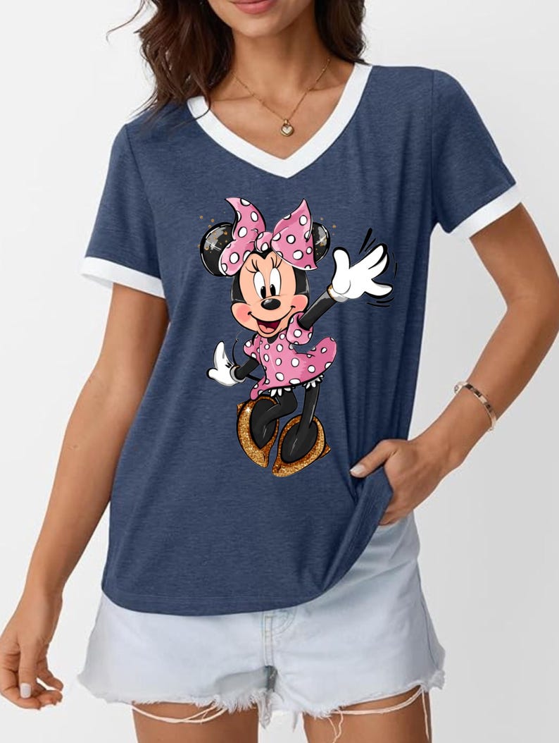 K&ouml;nnte beinhalten: Marineblaues V-Ausschnitt-T-Shirt mit wei&szlig;em Besatz und einem Cartoon-Bild von Minnie Mouse. Minnie Mouse tr&auml;gt ein rosa gepunktetes Kleid, eine Schleife und Schuhe. Das Shirt ist ein l&auml;ssiger Stil.