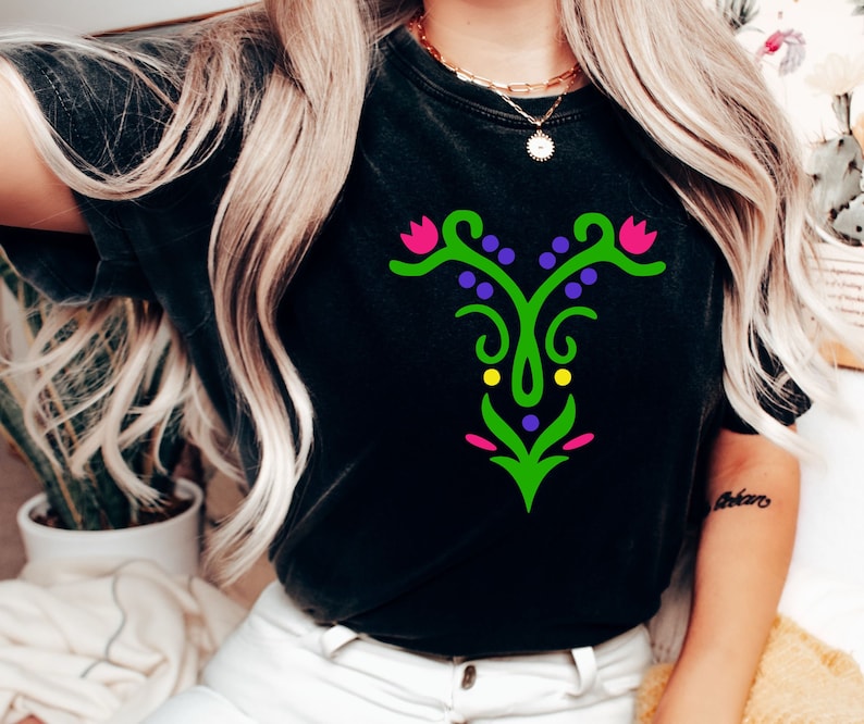 May include: Black t-shirt with a green, pink, and purple floral design. The design features a stylized flower with a stem and leaves.