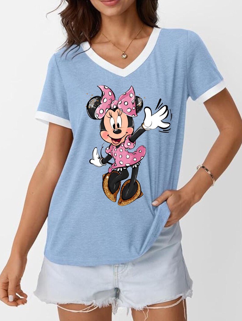 K&ouml;nnte beinhalten: Hellblaues V-Ausschnitt-T-Shirt mit wei&szlig;em Besatz und Minnie Mouse-Grafik. Minnie tr&auml;gt ein rosa gepunktetes Kleid und eine Schleife mit goldenen Glitzerschuhen. Ein l&auml;ssiger Stil.