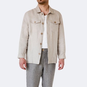 Könnte beinhalten: Eine beige Leinenjacke mit einem weißen T-Shirt darunter, graue gestreifte Leinenhose und weiße Sneaker mit grünen und blauen Akzenten.