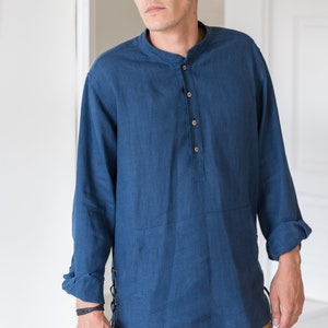 Op de afbeelding: Een blauw linnen overhemd met een mandarijnkraag en lange mouwen. Het overhemd heeft een knoopsluiting en een kantdetail aan de zijkant. Het model draagt het overhemd met een bruine broek.