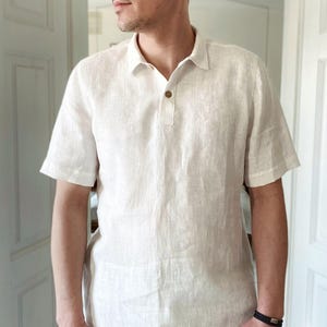 May include: A white linen short-sleeved shirt with a button-down collar and a single button closure. The shirt is made of a lightweight, breathable fabric and has a relaxed fit.