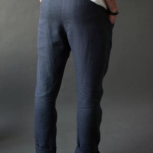 A man standing in the dark background, showing the back view of classic linen pants with two back pockets and a slightly tapered fit